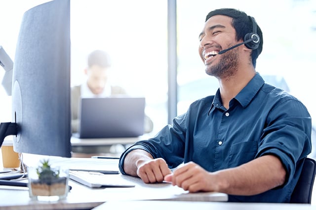 Smiling professional man sits at desk with computer wearing a headset