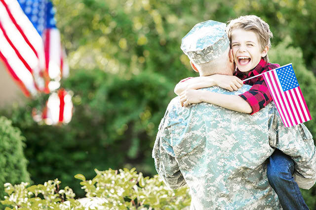 Service member hugs child holding an American flag. 